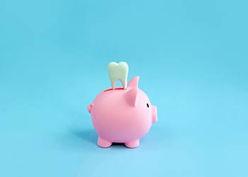 A model tooth placed over a pink piggy bank in a blue setting