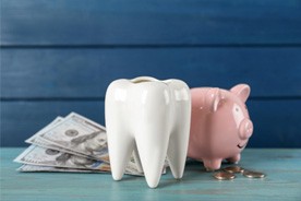 A ceramic model of a tooth next to a piggy bank and dollar bills