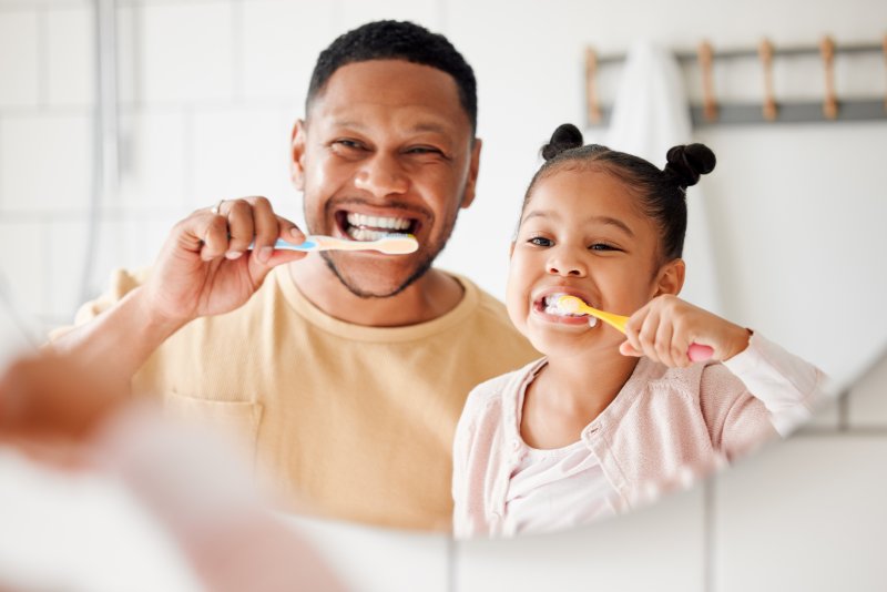 A man brushing his teeth with his daughter preparing for their early dental checkups