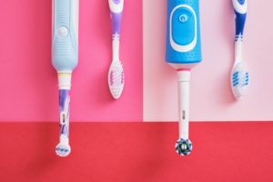Electric and manual toothbrushes on a pink and red background